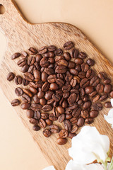 Coffee beans are scattered on a wooden board on a brown background. 