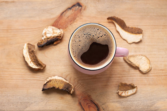 Mushroom Coffee Chaga Superfood. Dried Mushrooms And Fresh Brewed Pink Cup Of Hot Drink With Foam On Wooden Background Top View. Healthy Organic Energizing Adaptogen, Endurance Boosting Food Trends.