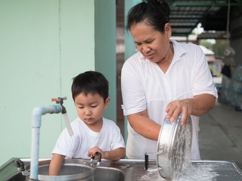 Asian Little Child Boy Helping Grandmother Wash Pot With Happy Smiling Face And Relaxing Family Time Together. Kid Learning To Clean Pot, Doing Housework. Ef Concept.