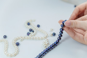 Close-up of hand of needlewoman making necklace of natural pearls