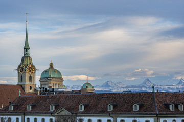 Blick auf das Bundeshaus und Heiliggeistkirche im Abendlicht vor Bergkulisse – Bern, Schweiz	