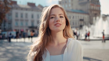 Portrait of pretty young woman with frizzy hair in city center smiling and looking at camera enjoying urban city having fun sun is shining