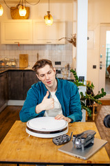 handsome intelligent man blogger presenting device at camera, sit in front of camera and talk. blogging concept. indoors