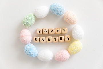 The words Happy Easter made with wooden cubes with letters together with colorful eggs on a white background