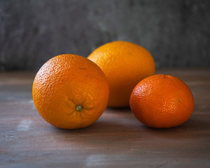 Oranges and one tangerine lie on a roughly painted table. Close-up