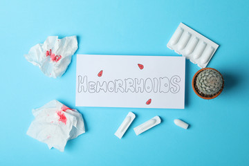 Inscription Hemorrhoids, candles, cactus and paper with blood on blue background