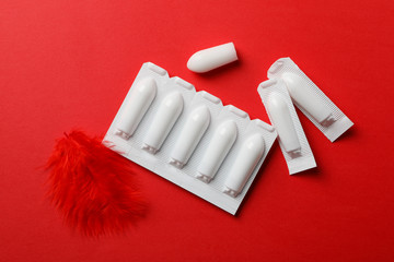 Anal or vaginal candles and feather on red background, top view