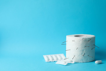 Toilet paper with nails and candles on blue background. Hemorrhoids