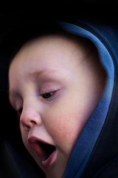 Closeup face portrait from the side of cute little child wearing a hoody.  Moody dark black background.