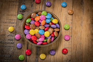 Colorful candies in a wooden bowl case isolated on wood background