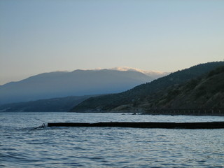 Breakwater on the shore of a calm sea against the background of coastal mountains in the haze of the sky in the distance in the evening.