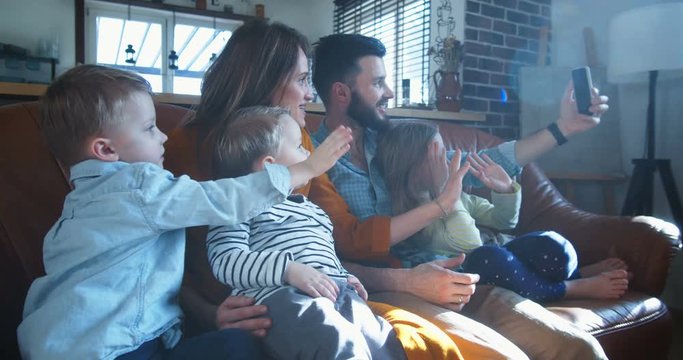 Happy young European family with children chatting with friends during smartphone online video call at home slow motion.