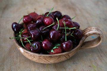 Cherry and garden strawberries in a ceramic clay cup on a wooden table. Vitamin summer snack