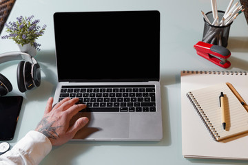 Freelance work.Hand man sitting at a glass table indoors, working on a laptop with notepad, mobile and headphones. Telework concept