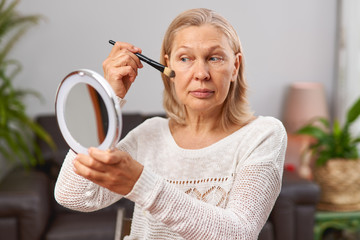 Beautiful senior woman after applying make up holding a brush.