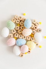 The words Happy Easter made with wooden cubes with letters together with colorful eggs on a white background