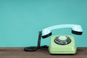 Old telephone on wooden table in front of green background. Vintage phone with taken off receiver....