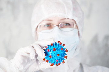 woman in protective suit holds coronovirus model