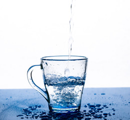 A stream of water pours into a glass Cup on a white background.