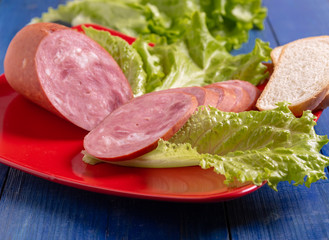 Slices of sausage, wheat bread and lettuce on a plate on the table close-up.