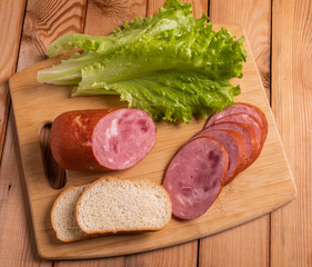 Slices of sausage, wheat bread and lettuce on a plate on the table close-up.