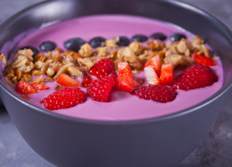 Smoothie bowl with berries and muesli on the gray table.