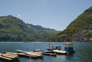 Boat piers on Lake Lugano, Switzerland. Alpine mountains covered with green plants in the background.