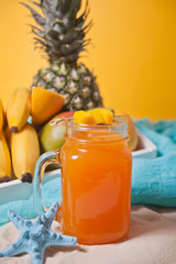 Glass of tropical exotic multifruit juice on the beach with fruits on the background. Tropical picnic.