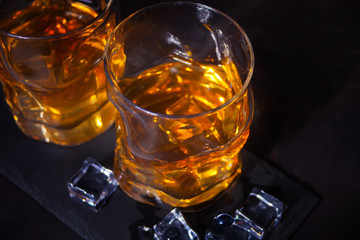 Two glasses of whiskey with ice on a black table.