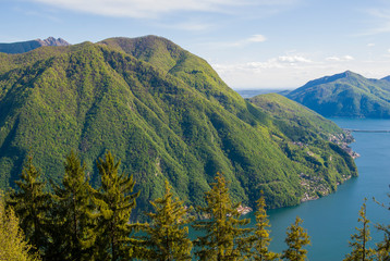 A top view of Lake Lugano, Switzerland from the height of Mount Monte Bre. Beautiful mountain scenery on a sunny summer day. View of Lake Lugano and the Alpine mountains covered with green plants.