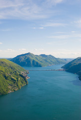 A top view of Lake Lugano, Switzerland from the height of Mount Monte Bre. Beautiful mountain scenery on a sunny summer day. View of Lake Lugano and the Alpine mountains covered with green plants.