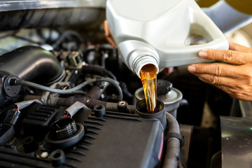 Car mechanic replacing and pouring fresh oil into engine at maintenance repair service station. - obrazy, fototapety, plakaty