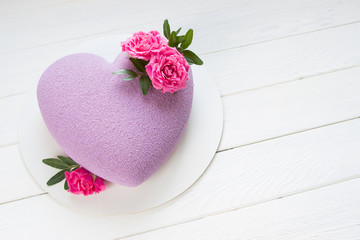 Modern  mousse cake .Heart shape  cake covered with purple chocolate velour and decoraited of pink roses.White wooden board.Concept for Wedding , St. Valentine's Day, Mother's Day, Birthday Cake.