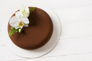 Trendy mousse cake covered with   chocolate velvet decorated white  flowers.White background, empty space. Concept for Wedding , St. Valentine's Day, Mother's Day, Birthday Cake. Brown cake