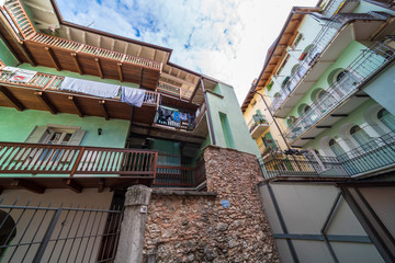 Rovereto, Italy street blue sky in small historic medieval town village in Trento looking up low angle vertical view during sunny summer day multicolored colorful painted walls and balcony