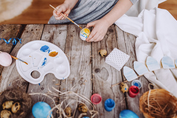 Happy easter! Cute little child girl painting with blue and yellow colors Easter eggs. family preparing for Easter. Hands of a girl with a easter egg. close-up