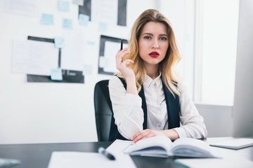 young blond beautiful woman manager with red lipstick works in her modern office, holding pen in her hand, looks sexy, multitasking, work concept