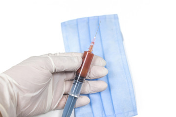 Doctor holding medical syringe with blood and a medical mask on a white background