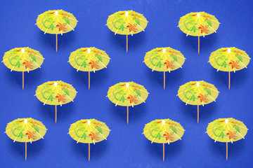 Fototapeta na wymiar Summer concept with yellow paper cocktail umbrellas on blue background