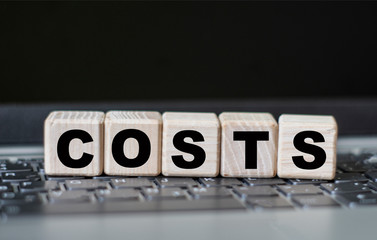 concept word COSTS on cubes against the background of laptop keys