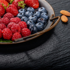 Tray with ripe organic bilberry raspberry strawberry and almonds set on slate closeup