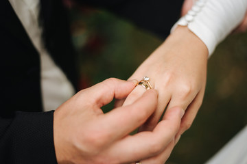 bride and groom holding hands; the groom puts a ring on the bride’s finger;  hands at the wedding ceremony;  ring exchange