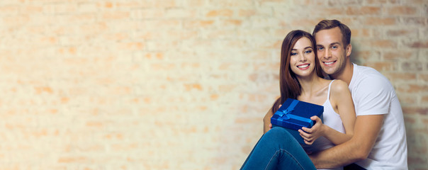 Portrait of beautiful amorous smiling couple holding blue gift box. Love, relationship, dating, happy lovers, concept, over loft style wall. Copy space for some text.