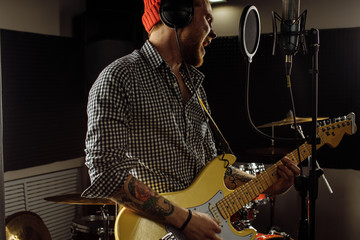 Obraz premium young talented caucasian musician play guitar and sing on microphone, professional guitarist preparing for rock concert in recording studio. music, instruments concept
