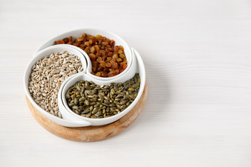 Peeled sunflower seeds, pumpkin seeds and raisins lie on a white table in a beautiful round plate divided into compartments, top view. Organic, vegetarian products that increase the body 's immunity