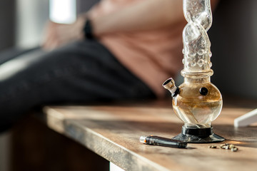 close-up photo of bong bottle with marijuana, lighter and hemp medicine on table. drug addiction,...