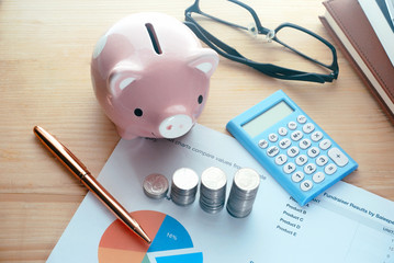Coins stack with calcuator and piggy save money and pen on document paper on working table,banking concept.