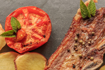 Grilled steak detail with legs and tomato on stone plate. American food concept