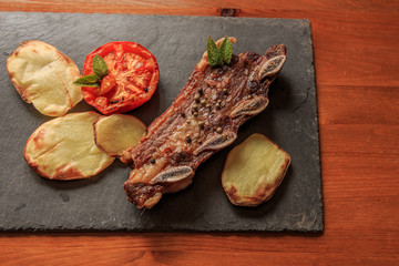 Grilled steak with legs and tomato on stone plate with wooden table. American food concept