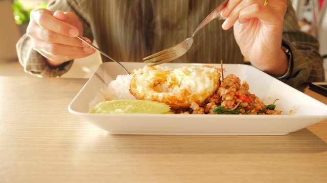 Slow-motion video of a Thai woman eating lunch at a food court in a department store. She is using a spoon to scoop steamed rice and fried eggs into her mouth.